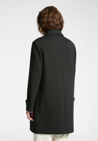 Abrigo negro con un cuello estructurado, mangas largas y corte recto. Textura suave y diseño minimalista sin patrones visibles.