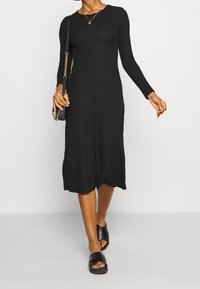 Svart ribbade långärmad klänning med figurnära bodice och utsvängd nederkant, tillsammans med svarta sandaler med öppen tå och klack samt en liten axelremsväska.