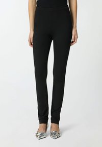 Leggings negros ajustados con cintura elástica, textura suave y diseño elegante, combinados con zapatos metálicos de punta afilada.
