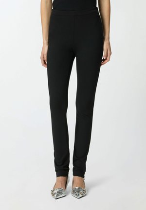 Leggings neri aderenti con coulisse elastica in vita, texture liscia e design elegante, abbinati a scarpe metallizzate con punta appuntita.