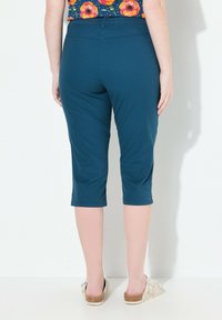 Pantalons cropped teal en tissu doux, avec une taille élastique et une texture lisse, assortis à des chaussures à enfiler de couleur claire.