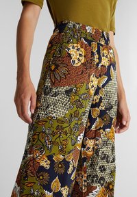 Pantalon à jambes larges à motifs avec des couleurs vertes, orange et bleu marine. Ceinture élastique avec différents motifs floraux et abstraits en textures contrastées.