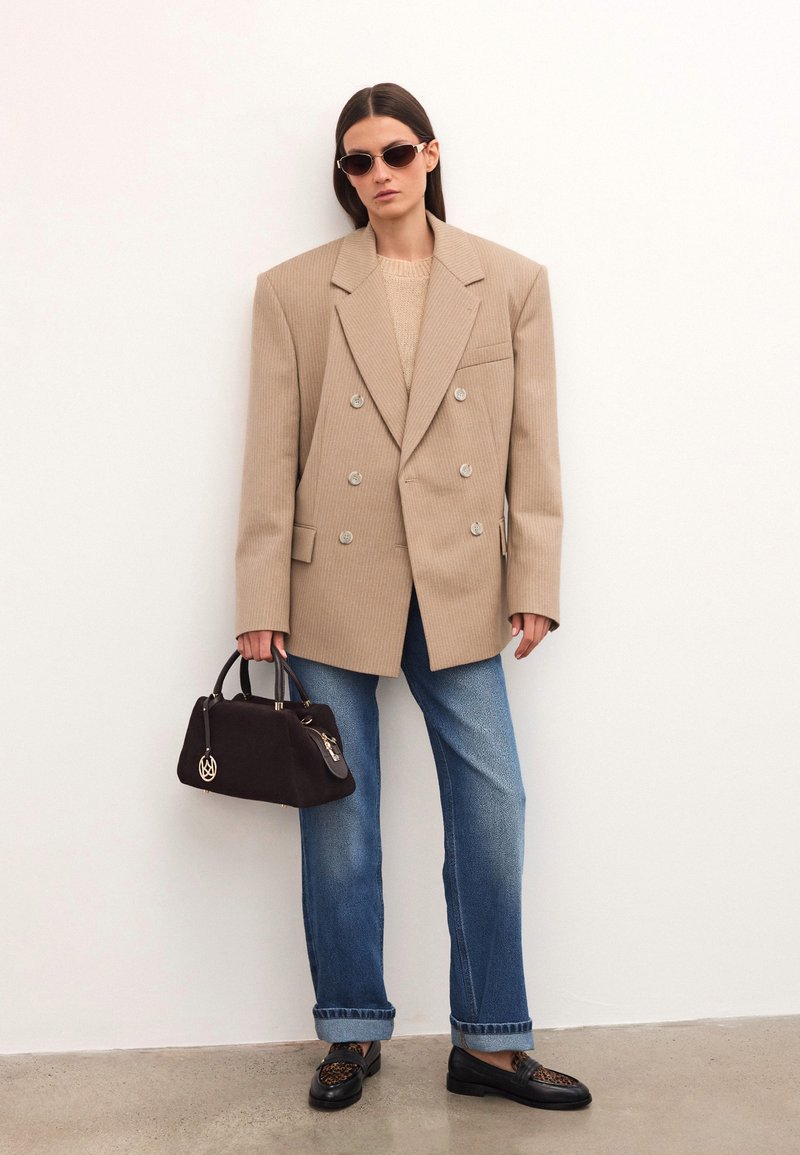 Naine kannab ülekaalu beezist triibulist bleiserit, siniseid teksaseid, musti leopardimustriga mokassine, prille ja hoiab musta käekotti.