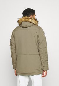 Giacca parka color khaki con cappuccio foderato in pelliccia, caratterizzata da una superficie liscia, chiusura a zip e tasche laterali. La vista posteriore mostra dettagli minimi.