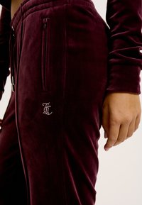 Bordeaux velours joggers hebben een slim fit, zijzakken en een decoratieve logo van rhinestones op de bovenbeen. Zachte textuur en elastische taille.
