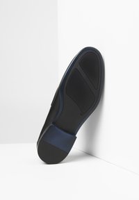 Suola di scarpa nera con grip in gomma, superficie testurizzata e sottili accenti blu. Presenta un tallone a contrasto e un design multi-segmentato.