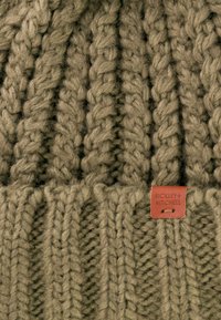 Olivgrüner Strickbeanie mit dicken, strukturierten Garnen und geripptem Design. Enthält ein kleines Lederschild mit der Marke "BICKLEY+MITCHELL".