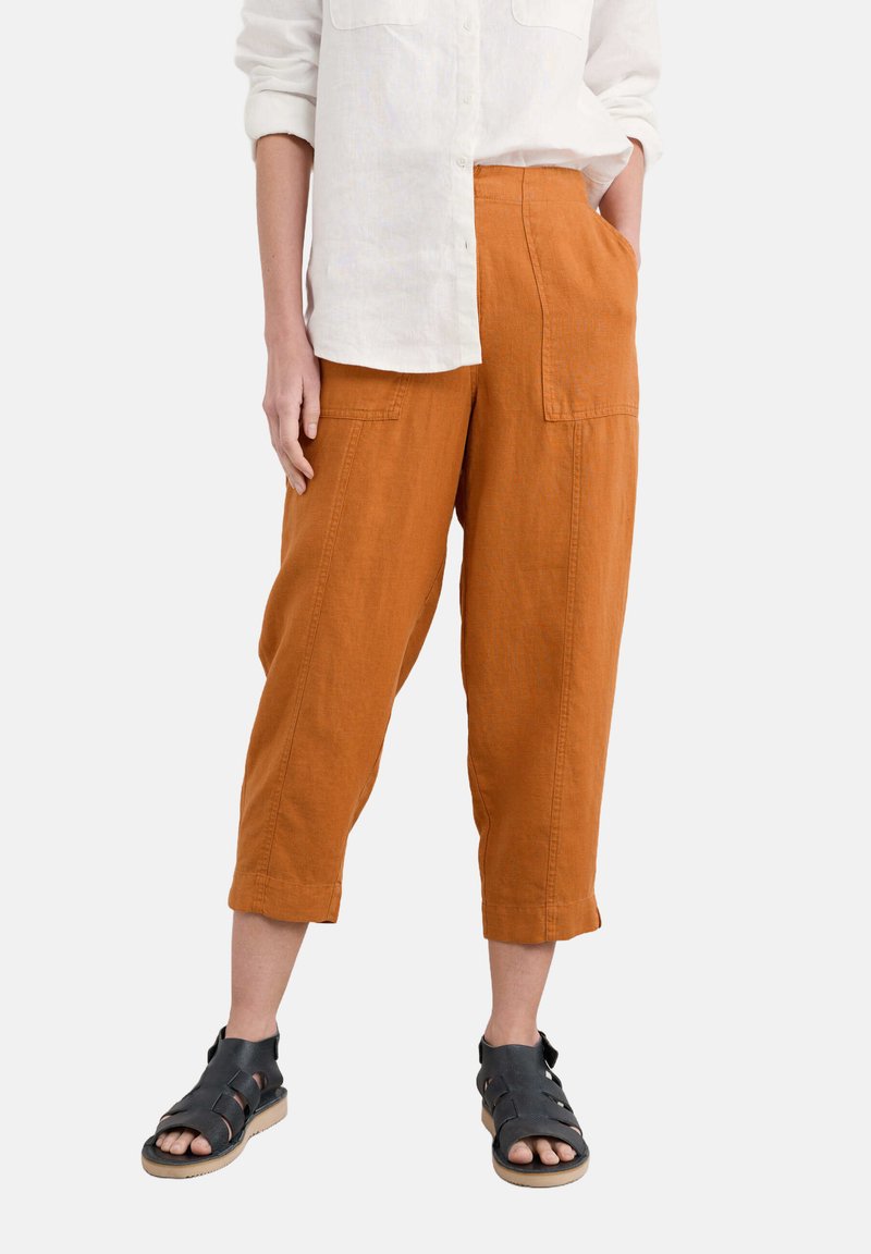Rust-colored linen cropped pants feature a loose fit, wide legs, and patch pockets. Paired with a white button-up shirt and black sandals.