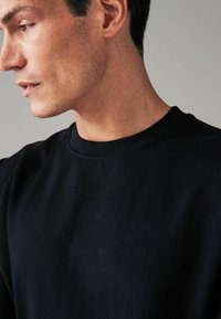 Zwarte katoenen t-shirt met een ronde hals, korte mouwen en een zachte textuur. Close-up weergave toont stiksels en huidskleur.