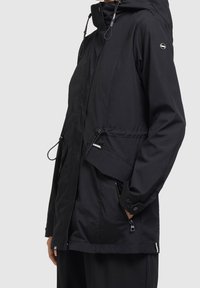 Musta vedenpitävä takki hupulla, jossa vetoketju, etutaskut ja kiristysnauha. Sileä pinta ja rento istuvuus.