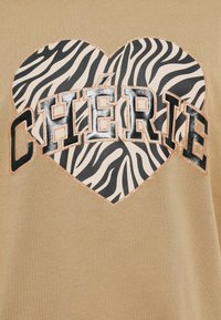 Χακί κοντομάνικο πουκάμισο με μεγάλο γραφικό καρδιάς με σχέδιο ζέβρας και τη λέξη "CHÉRIE" σε έντονα μαύρα γράμματα με χάλκινα γκλίτερ.