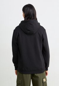 Czarna bluza z kapturem o luźnym kroju, z prążkowanymi mankietami i dolnym wykończeniem. Noszona z oliwkowozielonymi spodniami cargo, prezentująca swobodny styl streetwear.