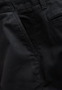 Close-up of black fabric pants showing front pocket, belt loop, and stitching details.