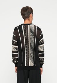 Strikket sweater i sort, hvid og grå med mønstrede striber og teksturerede detaljer på ryggen; har en rund hals og lange ærmer.