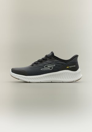 Chaussure de sport Skechers noire et grise avec semelle blanche, lacets noirs, logo "S" sur le côté et texte "SLIP-INS" près du talon.