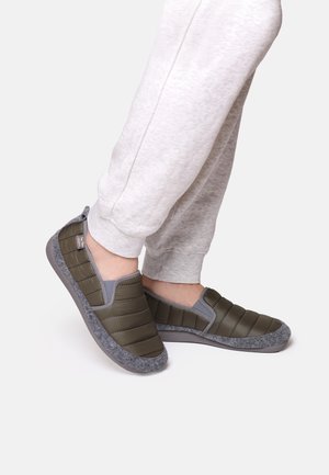 Chaussures vertes à enfiler avec un dessus matelassé, des accents gris et une semelle en feutre gris, accompagnées de survêtements gris clair.