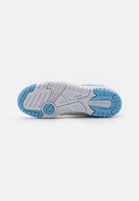 Shoe sole in light gray and blue, featuring textured rubber for grip, patterned tread, and branding details. Rounded shape for athletic use.