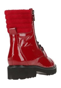 Bottine à cheville en cuir verni rouge avec poignet en tissu matelassé, fermeture éclair latérale, lacets noirs et semelle épaisse en caoutchouc noir.