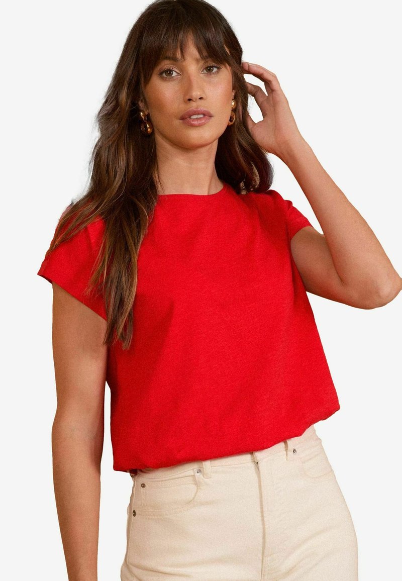 Top corto rojo de manga corta, hecho de una tela suave, con un escote redondo y un ajuste relajado, combinado con jeans de color claro.