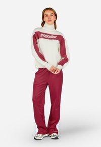 Biały sweter z bordowymi akcentami i logo "pegador", w zestawie z bordowymi spodniami dresowymi z białymi paskami po bokach i teksturowanymi sneakersami.
