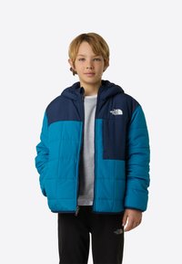 Μπουφάν-φουσκωτό σε μπλε και ναυτικό μπλε χρώμα με κουκούλα, που έχει μπροστινό φερμουάρ, καπιτονέ υφή και λεπτομέρεια λογότυπου στο στήθος και στο μανίκι.