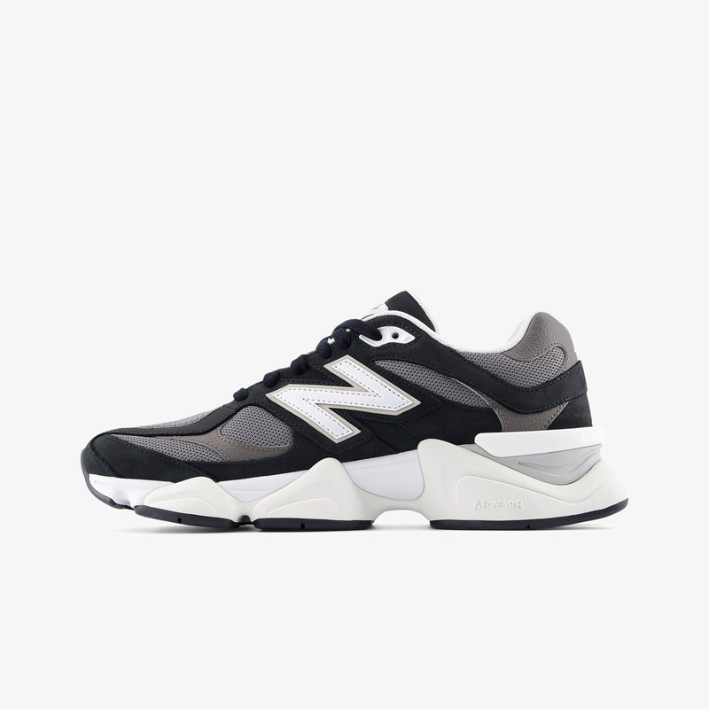 Μαύρο και γκρι αθλητικό παπούτσι New Balance με λευκό λογότυπο "N", μαξιλαρωτή λευκή σόλα και επάνω μέρος από δίχτυ και σουέτ, πλάγια όψη σε λευκό φόντο.