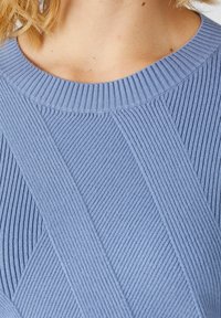 Maglione a coste di un blu chiaro con un design testurizzato, dotato di scollatura arrotondata e motivi di cuciture diagonali. Tessuto morbido e lavorato a maglia.