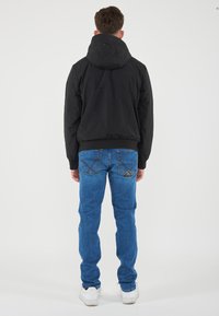 Black jacket with a hood, paired with blue jeans. The jacket has a smooth texture, while the jeans feature back pockets with stitching details.