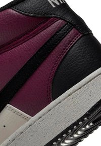 Zapatillas de alta caña con un diseño de materiales mixtos en negro, burdeos y crema, con superficies texturizadas y una suela de goma con un patrón distintivo.