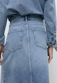 Denim krilo v svetlo modri barvi s ravno silhueto, ki vključuje dve zadnji žepki, vidno šivanje in subtilno teksturo.