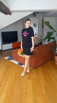Young woman posing in black Karl Lagerfeld Jeans dress and white flats in a modern living room with wooden floor and orange sofa.