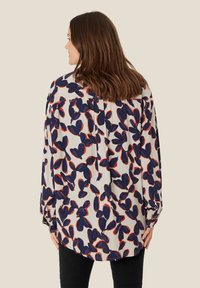 Blusa a maniche lunghe in tessuto leggero con motivo floreale in navy, rosso e bianco. Orlo arrotondato e polsini con bottoni.