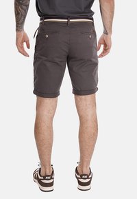 Pantaloni corti in cotone grigi con risvolti, dotati di due tasche posteriori con chiusura a bottone e una cintura a righe. Indossati con scarpe da ginnastica marroni.