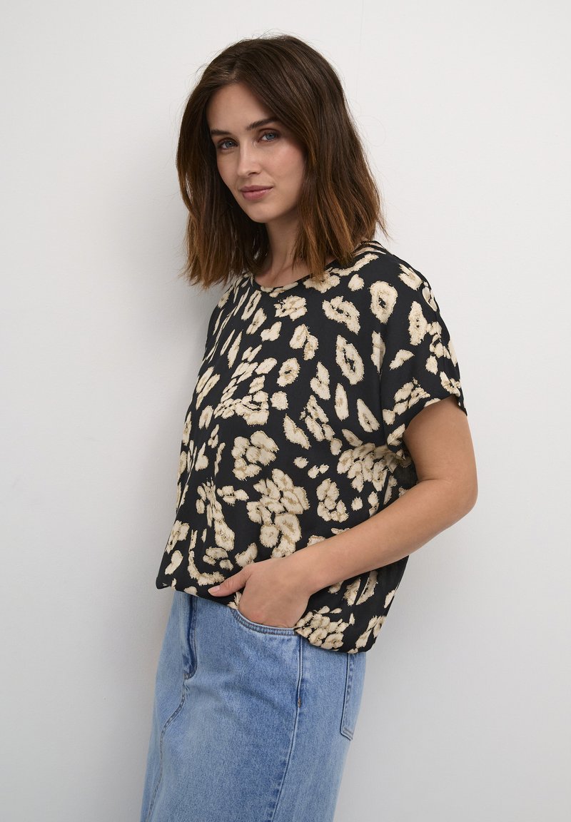 Blouse noir à manches courtes avec un motif floral beige. Dotée d'un col rond et d'une coupe décontractée, assortie à un jean en denim bleu clair.