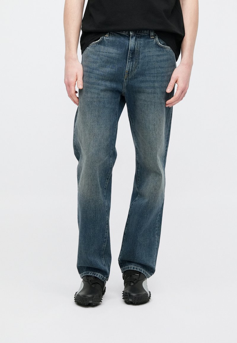 Faded blue denim jeans with a straight-leg cut, five pockets, belt loops, and a subtle wash pattern. Worn with black shoes.