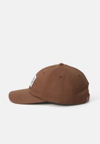 Căciulă de baseball din bumbac maro, cu brăcătură curbată, design cu șase panouri, orificii brodate și un eticheta pe față.