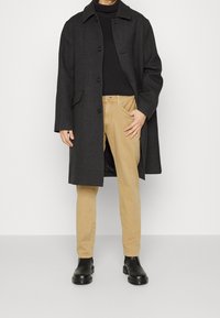 Tummanharmaa villakangastakki napituksella, sivutaskuilla, yhdistettynä beigepunaisiin housuihin ja mustiin nahkabootseihin. Kauluspaita alla.