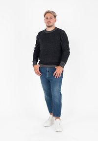 Maglione scuro a trama con colletto a coste, abbinato a jeans a sigaretta blu chiaro e sneakers bianche. Il modello posa su uno sfondo neutro.