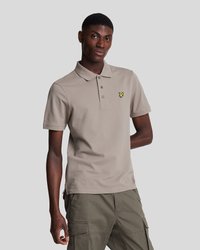Camisa polo beige con tapeta de tres botones y mangas cortas, que presenta un pequeño logo amarillo en el lado izquierdo del pecho, combinada con pantalones cortos cargo de color verde oliva.