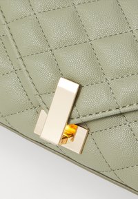 Borsa a tracolla in pelle verde trapuntata con chiusura rettangolare in tono oro, caratterizzata da una finitura testurizzata e dettagli di cucitura a contrasto.