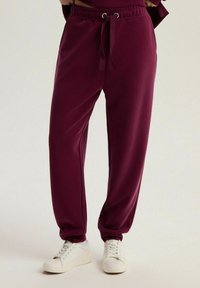 Bordowe dresy o luźnym kroju, z elastycznym pasem i sznurkiem. Wykonane z gładkiego materiału, z bocznymi kieszeniami. W połączeniu z białymi trampkami.