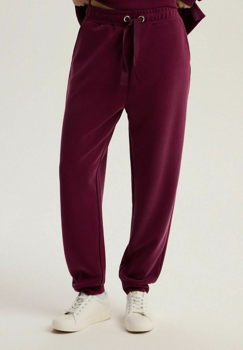 Bordowe dresy o luźnym kroju, z elastycznym pasem i sznurkiem. Wykonane z gładkiego materiału, z bocznymi kieszeniami. W połączeniu z białymi trampkami.