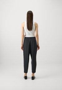 Pantalon sur mesure bleu marine foncé avec une coupe fuselée, associé à un débardeur blanc. Texture lisse et design minimaliste. Des chaussures noires sont portées.