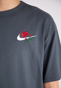 Gray cotton t-shirt featuring an embroidered red rose and green leaves alongside a white Nike swoosh logo on the upper left.