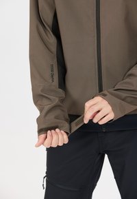 Braune, leichte Jacke mit glatter Textur, ausgestattet mit einem Reißverschluss, verstellbaren Bündchen und einem Logodetail am Ärmel.