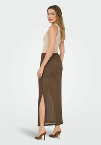 Bruine mesh maxi rok met een hoge split en textuurpatroon, gecombineerd met een beige mouwloos topje en bruine open teen hakken.