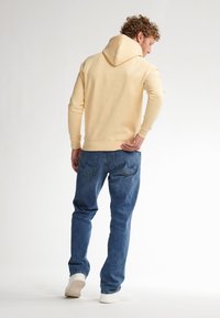 Felpa con cappuccio giallo chiaro, dotata di tasca a marsupio, abbinata a jeans in denim blu e sneakers bianche. Design semplice e casual, con una vestibilità comoda.