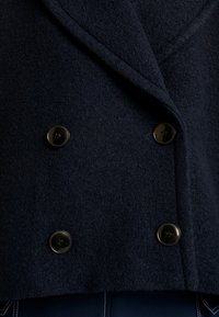 Marineblauwe wollen blendjas met een dubbelbreasted ontwerp, grote zwarte knopen, een uitgesneden kraag en een gestructureerd oppervlak.