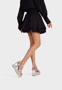 Sandali wedge metallici argento con una fascia glitterata, suola in juta intrecciata e chiusura alla caviglia. Abbinati a una gonna nera con volants.