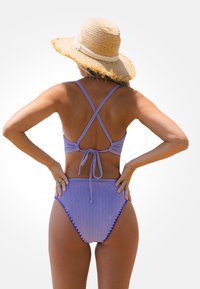 Paarse ribbelbikini met een striksluiting aan de achterkant en een high-waisted broekje, voorzien van gegolfde afwerkingen en kruislings straps voor extra detail.
